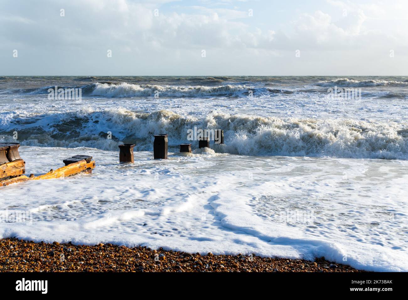 Onde che si infrangono sulla spiaggia di Bexhill-on-Sea con nuvole tempesta e una spiaggia groyne Foto Stock