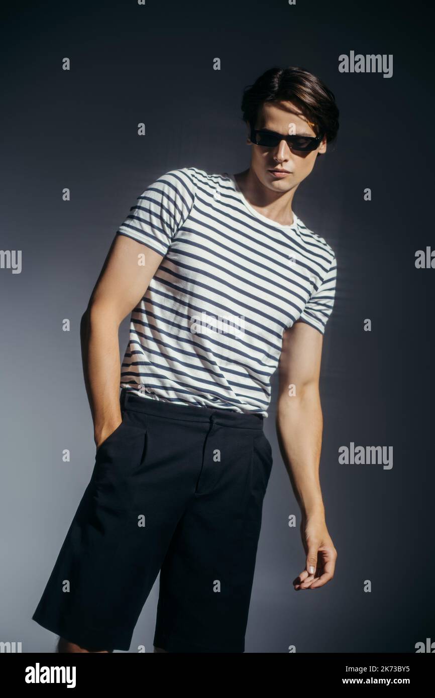 Modello in occhiali da sole e pantaloncini in posa su sfondo grigio con illuminazione Foto Stock