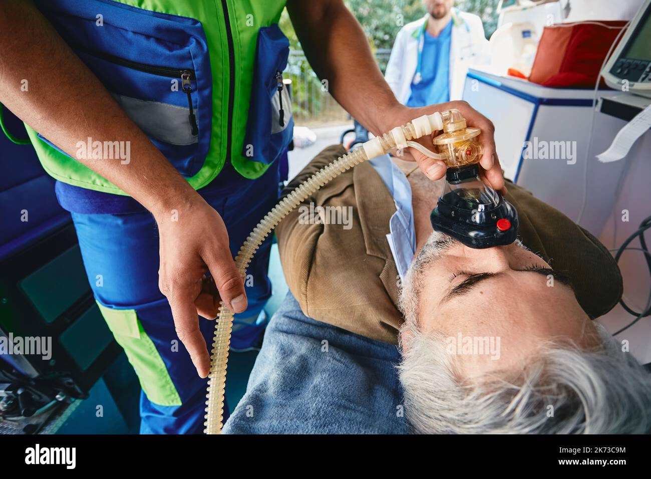 Paramedico maschile fornendo assistenza medica tenendo maschera di ossigeno sopra il viso del paziente sdraiato sul gurney all'interno dell'ambulanza. Trattamento ambulanza Foto Stock