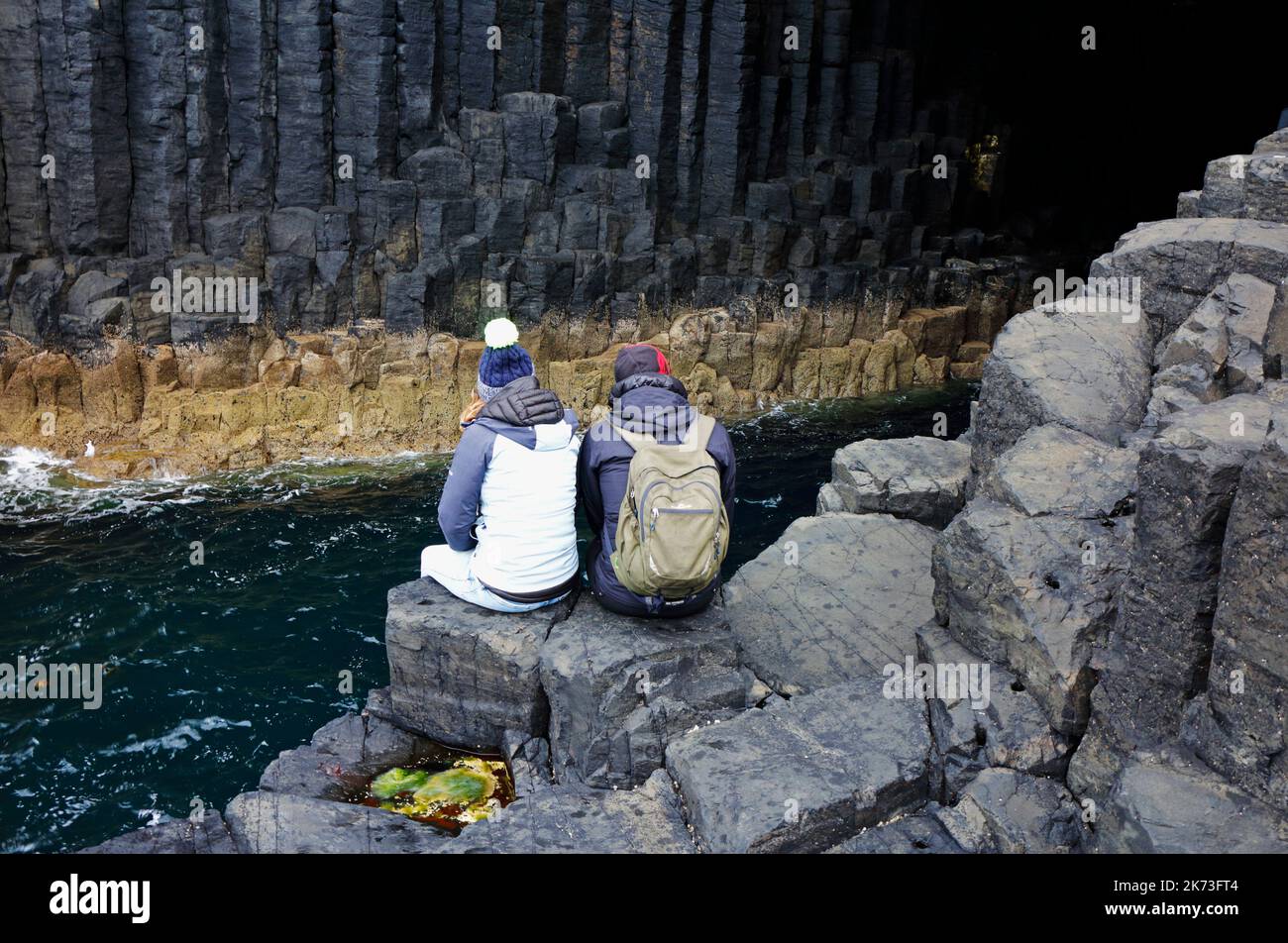 Due persone sedute sulle rocce all'ingresso della Fingal's Cave sull'isola di Staffa, Ebridi interne, Scozia. Foto Stock