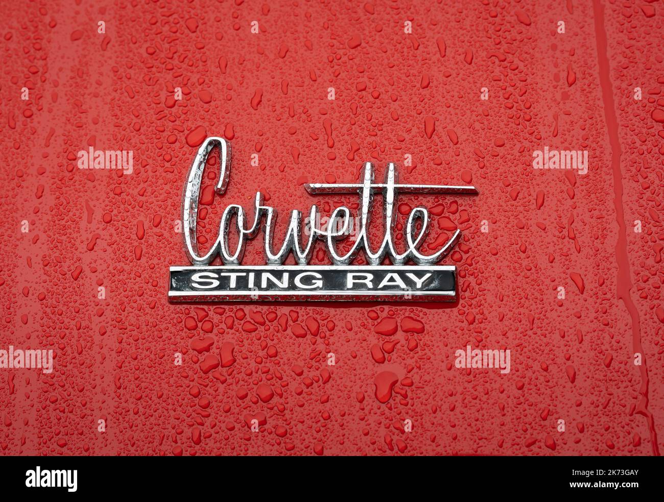 Brummen, Provincia Gelderland, Paesi Bassi, 15.10.2022, primo piano del segno Chevrolet Corvette Sting Ray con gocce d'acqua su sfondo rosso di Foto Stock