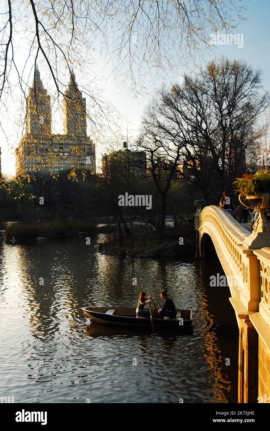 Un paio di file la loro barca a remi sul lago di Central Park sotto il ponte Bow e in vista del San Remo Apartments a New York City Foto Stock