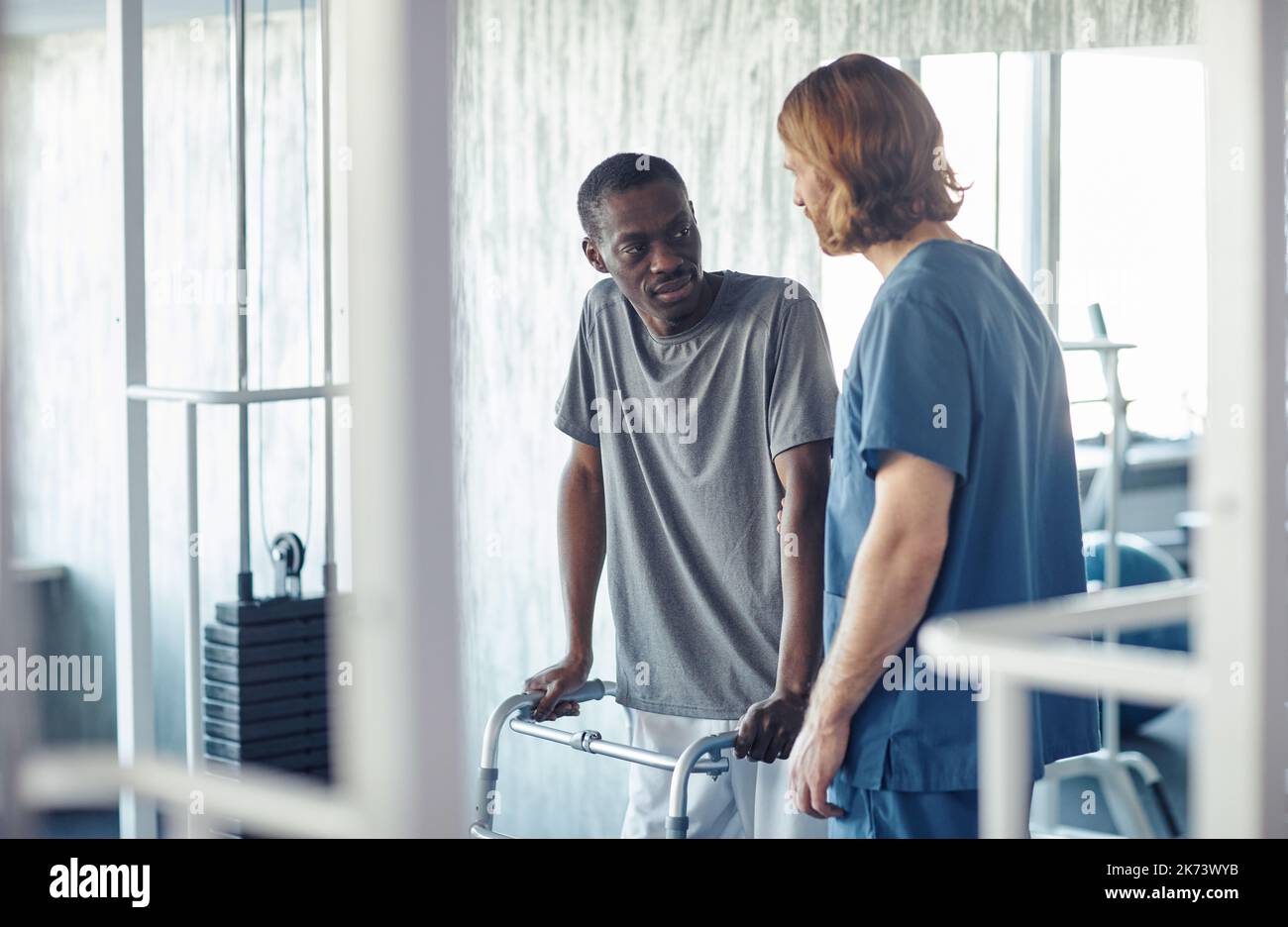 Paziente africano con disabilità che si esercita in palestra insieme al medico che lo aiuta Foto Stock