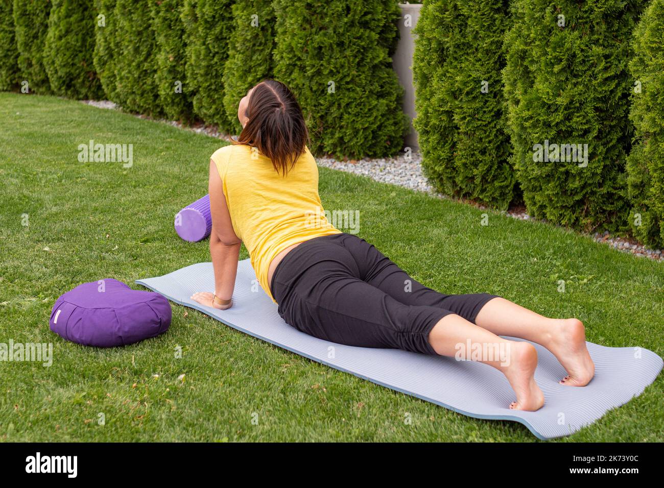 Donna che impara a praticare yoga sdraiato su una stuoia facendo asana per i principianti su un prato in estate Foto Stock