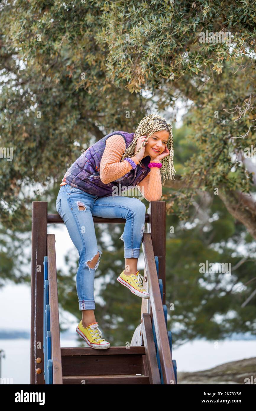 Donna matura in piedi su altalene in legno nel parco giochi parlando sul telefono smartphone e sorridendo felice Foto Stock