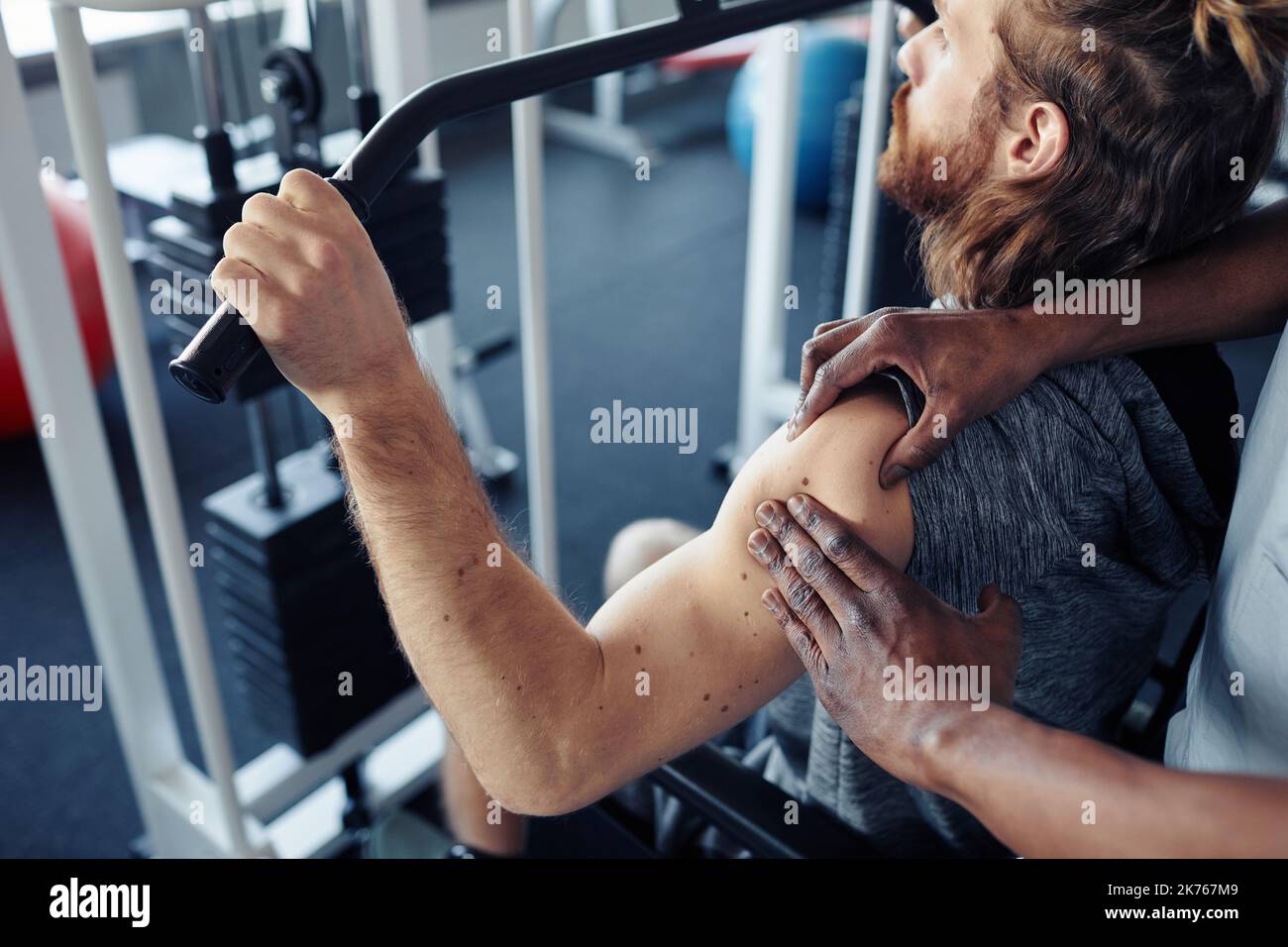 Giovane paziente allenando il suo braccio di lesione su attrezzature ginniche in palestra, mentre il terapista massaggiarlo Foto Stock