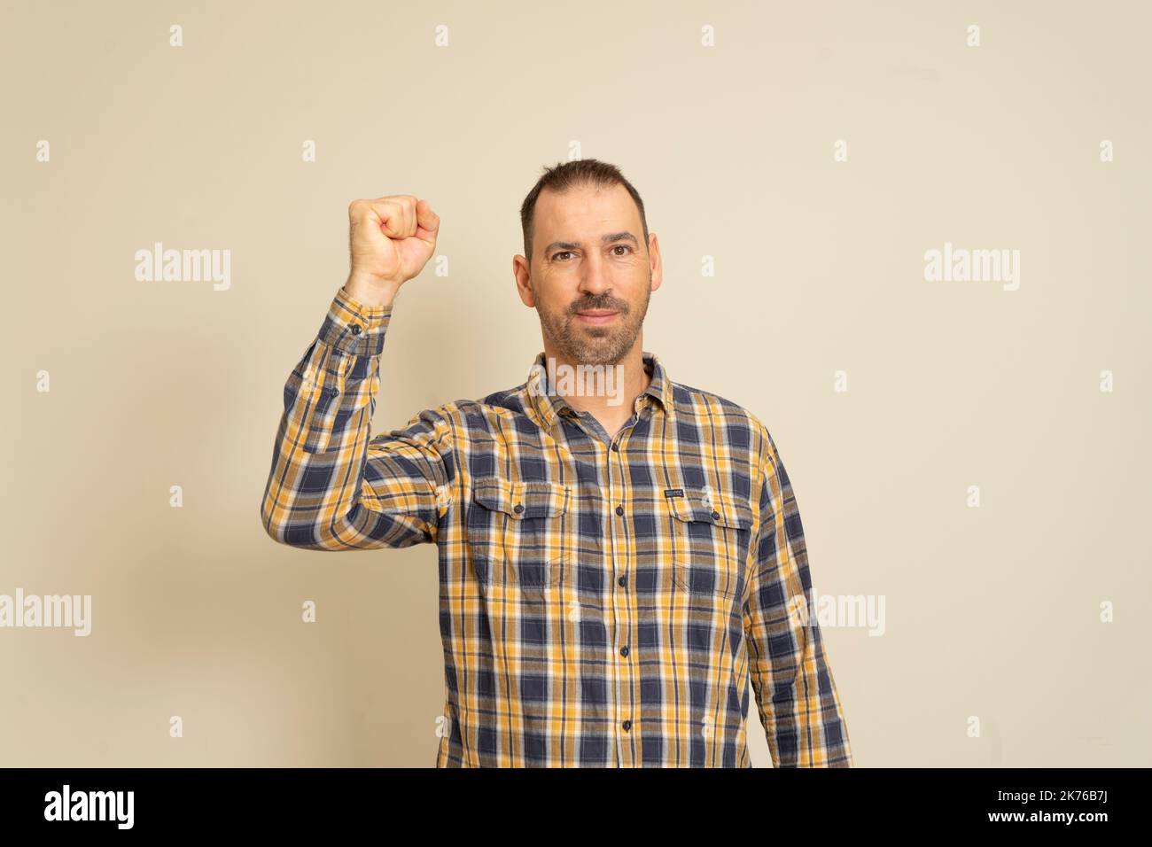 Felice riuscito businessman bearded che vince, pugno sollevato che celebra successo sfondo isolato della parete beige. Emozione umana positiva espressione facciale Foto Stock