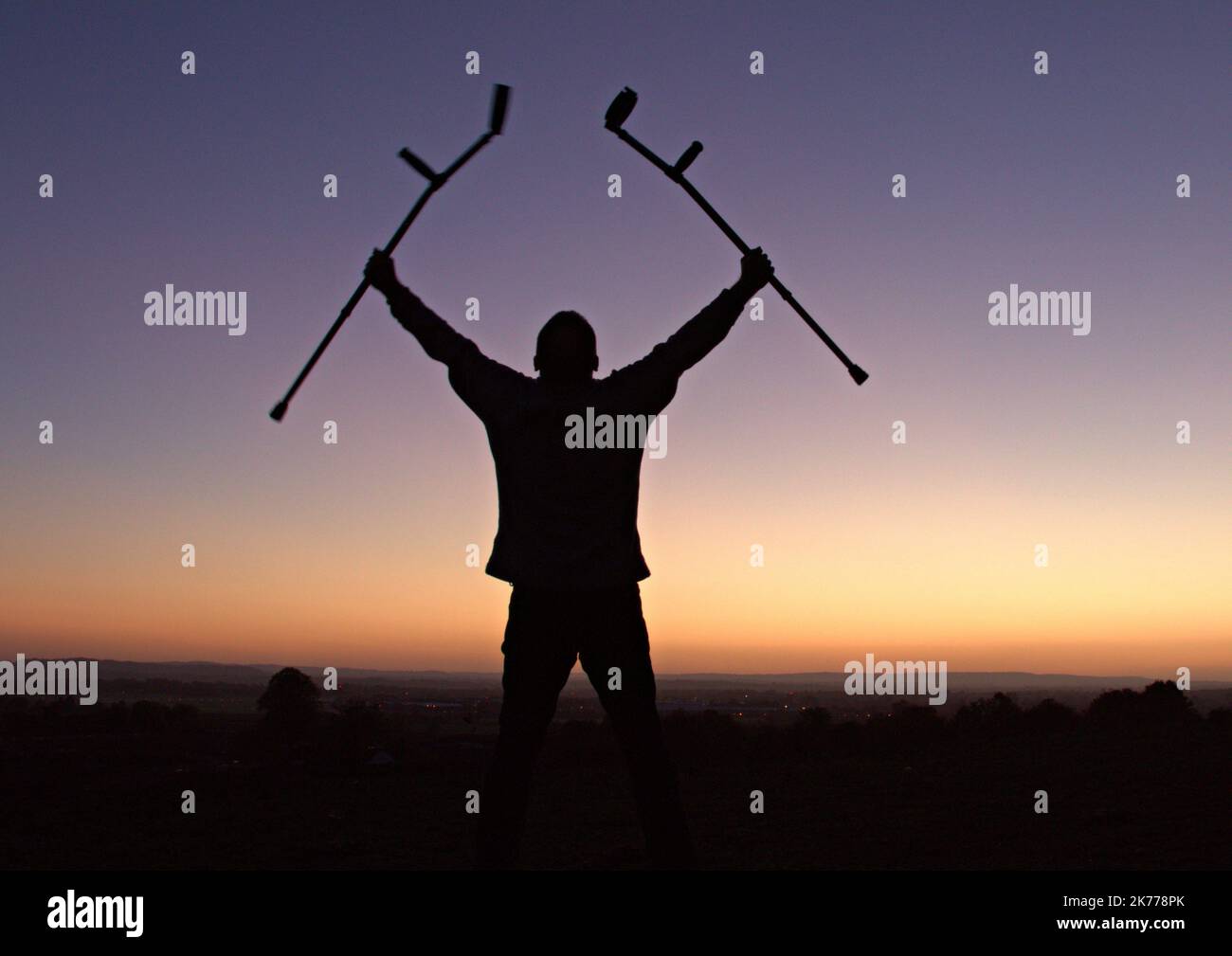 Silhouette di uomo che tiene le stampelle in aria con il tramonto dietro Foto Stock