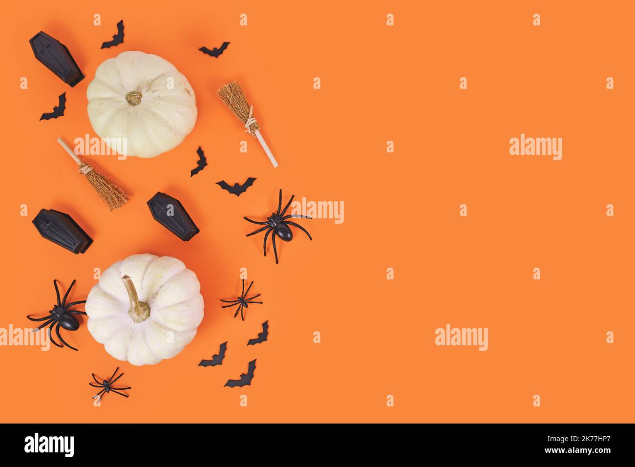 Composizione di Halloween con zucche bianche, ragni neri, pipistrelli e bare e scope di strega su sfondo arancione con spazio copia Foto Stock