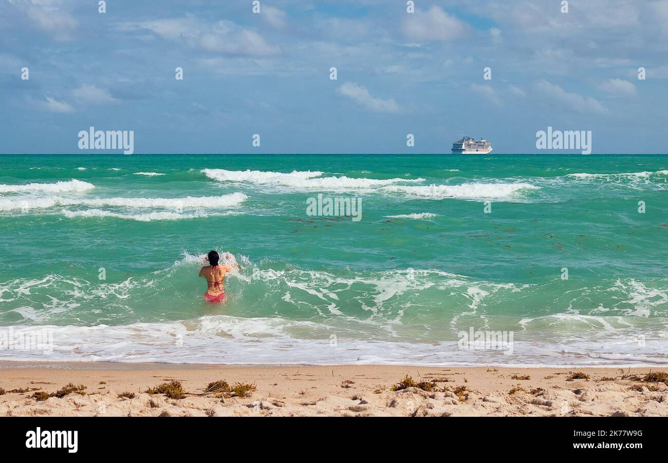 Una donna in costume da bagno rosso si immerge nell'oceano mentre una nave da crociera naviga via in lontananza. Foto Stock
