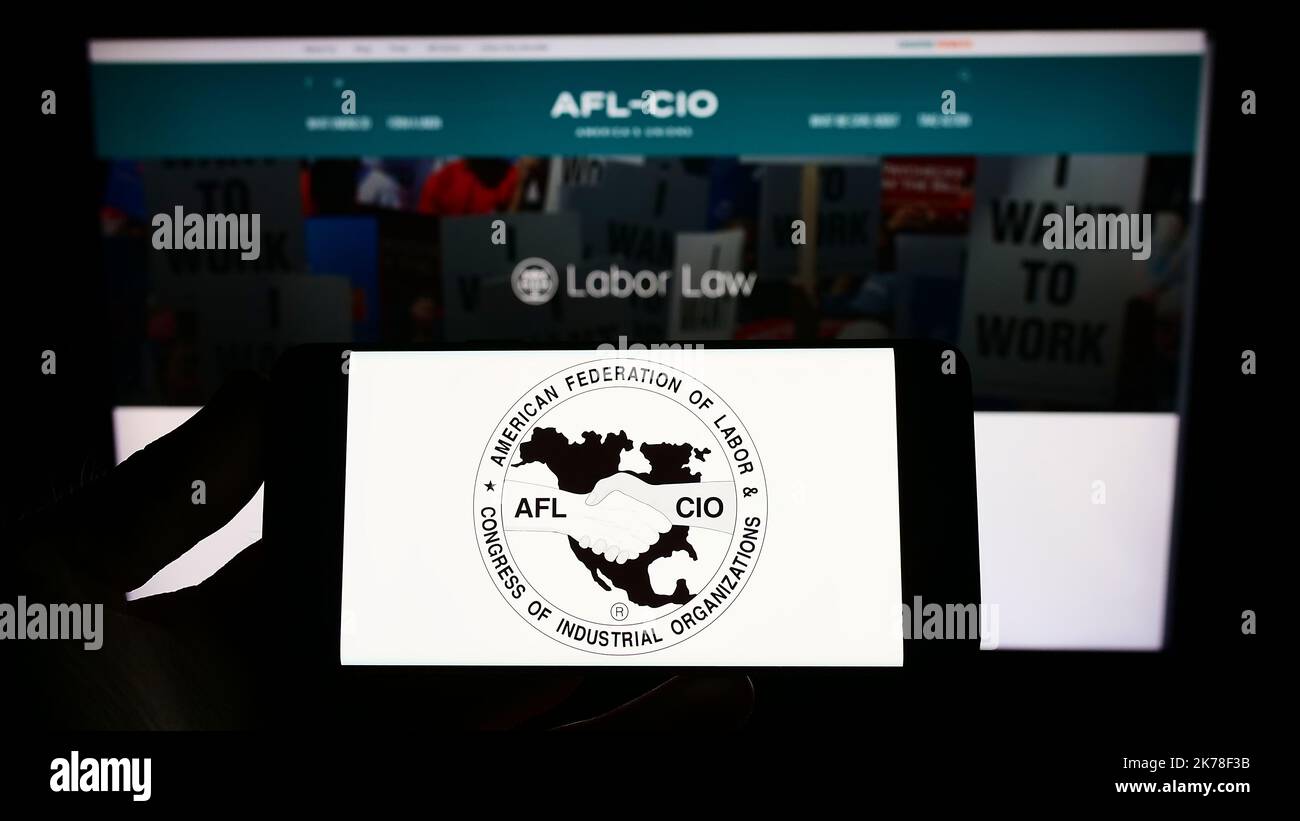 Persona che tiene il cellulare con il logo della federazione dell'Unione degli Stati Uniti AFL-CIO sullo schermo davanti al Web page. Messa a fuoco sul display del telefono. Foto Stock