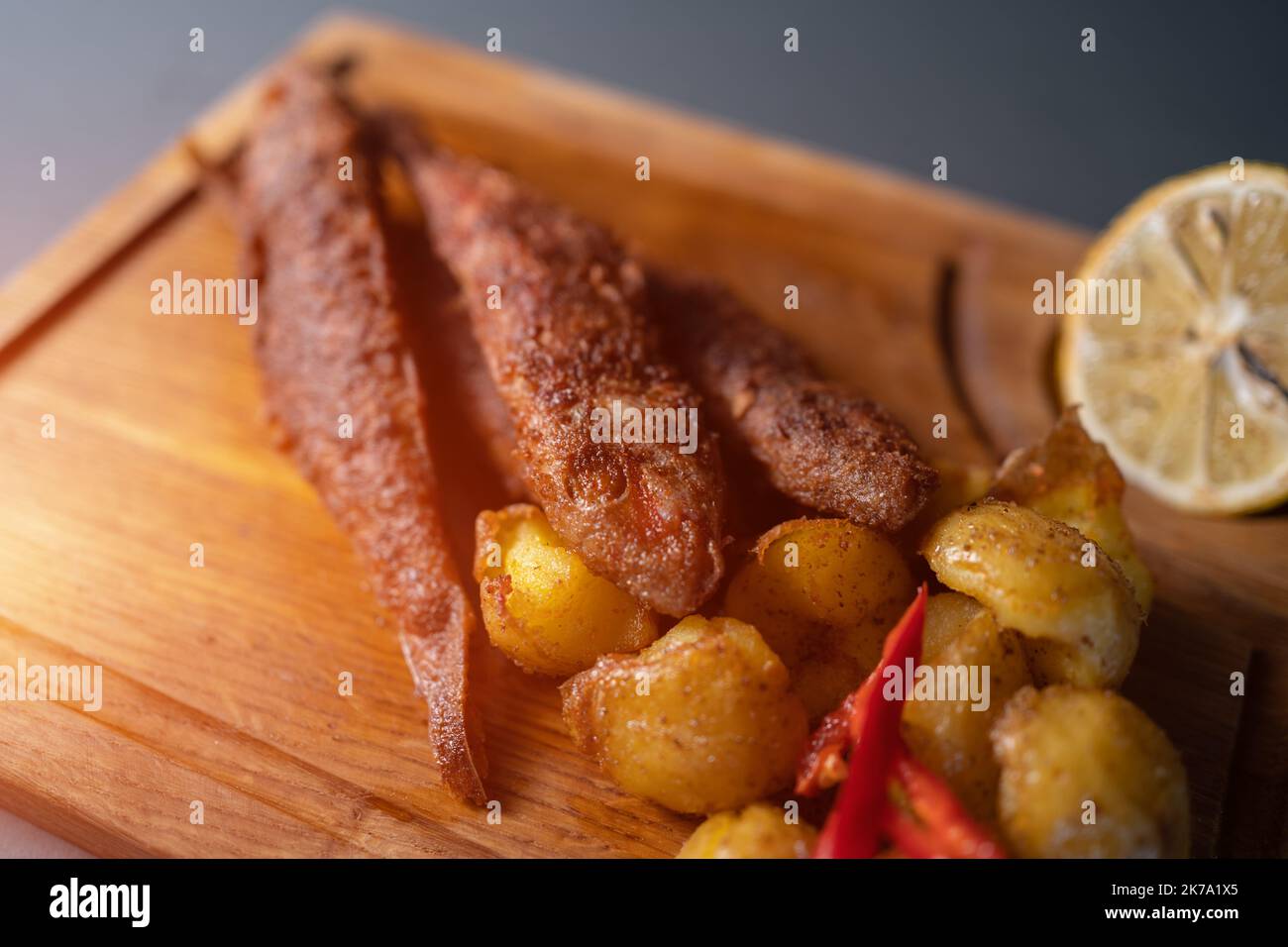 pesce surmullet fritto con patate e limone su tavola di legno su sfondo nero Foto Stock