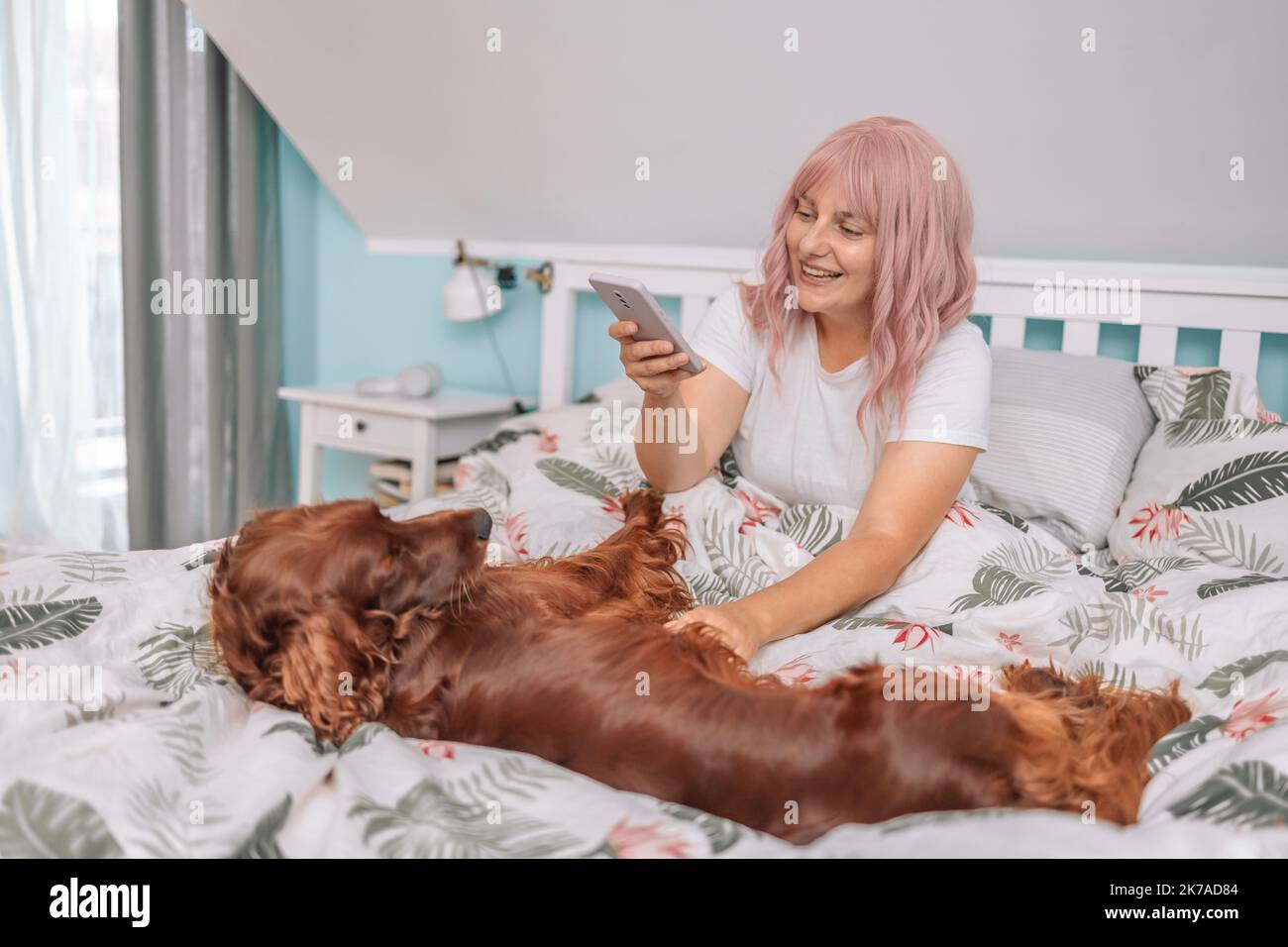 Bella giovane adulto giovane donna allegra prendere selfie su smartphone con il suo cane Irish Setter al mattino a letto Foto Stock