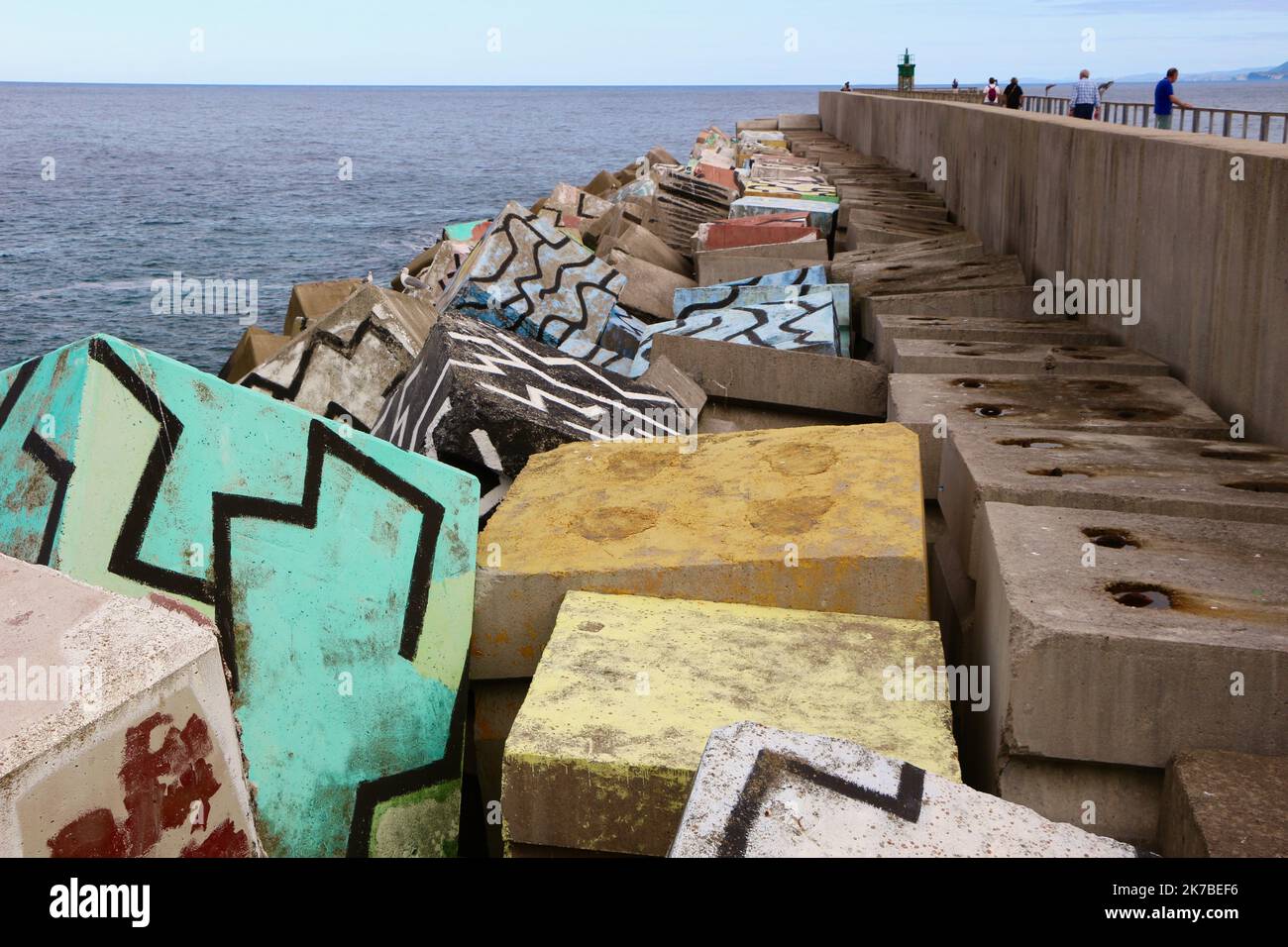 Ondate dissipando blocchi di cemento cubi di memoria dipinta da Agustin Ibarrola lungo la parete del porto di fronte al mare Llanes Asturias Spagna Foto Stock