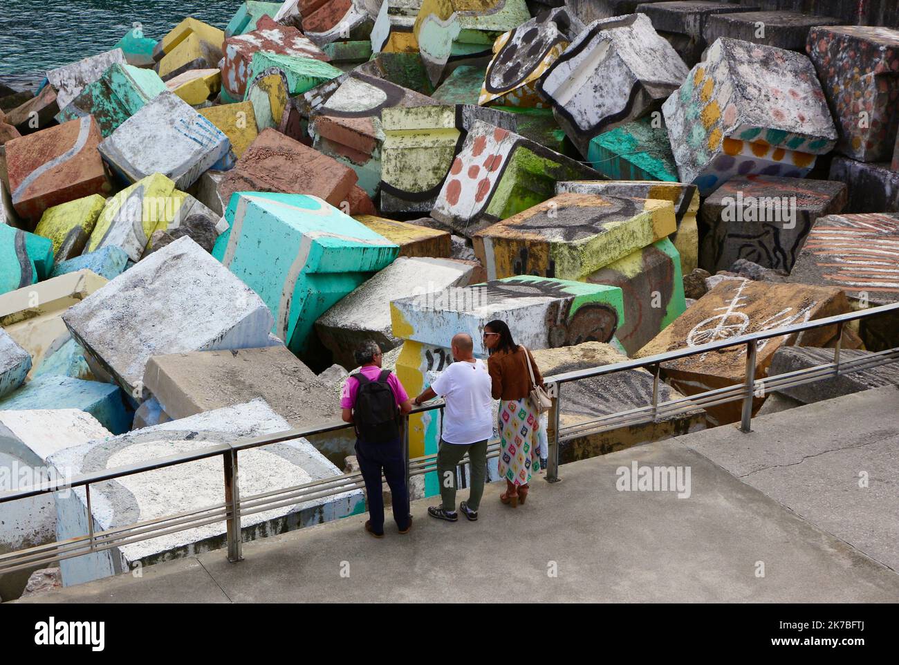 Tre persone che guardano l'onda dissipando blocchi di cemento cubi di memoria dipinta da Agustin Ibarrola ingresso al porto Llanes Asturias Spagna Foto Stock