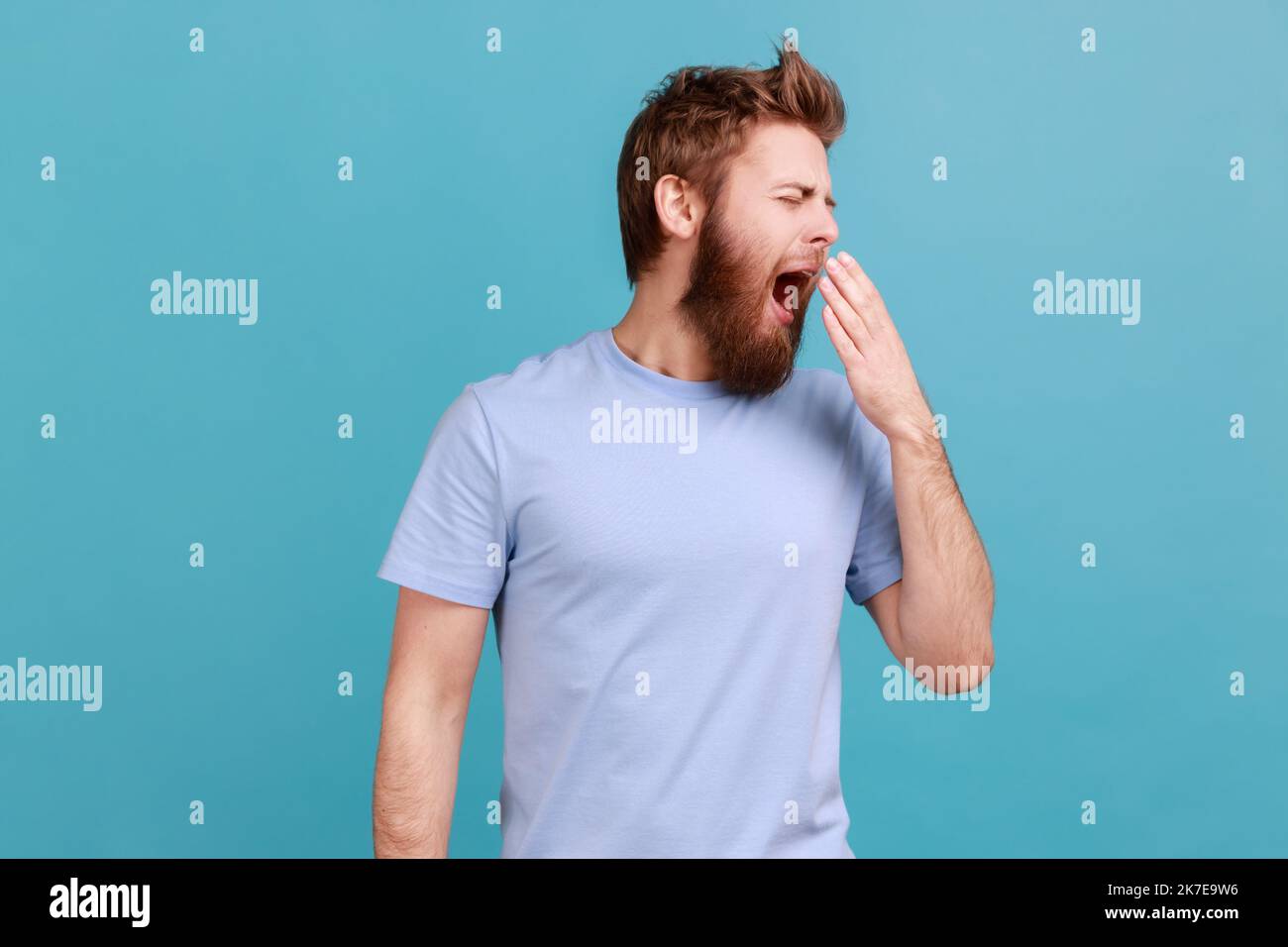 Bisogno di riposo. Ritratto dell'uomo bearato che urla e sogna il sonno, sensazione di sonnolenza, inefficienza nel fare lavoro, pigrizia e mancanza di energia. Studio in interni isolato su sfondo blu. Foto Stock