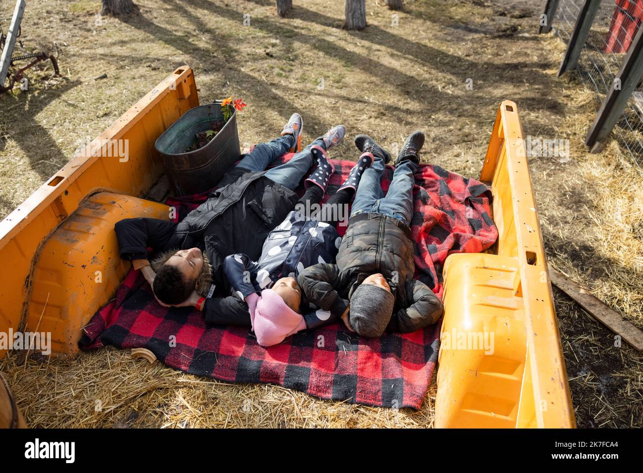 Fratelli e sorelle spensierati che stendono su coperta in letto di camion in fattoria Foto Stock