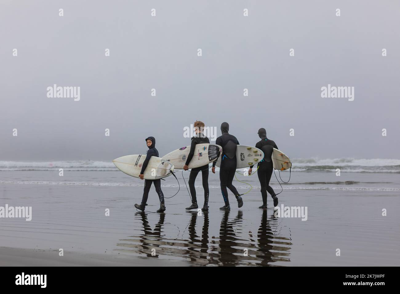 Gruppo di surfisti che trasportano le loro tavole da surf all'alba nebbiosa. Surfisti in mute alla spiaggia di Tofino Canada. Foto di viaggio, messa a fuoco selettiva, copyspa Foto Stock