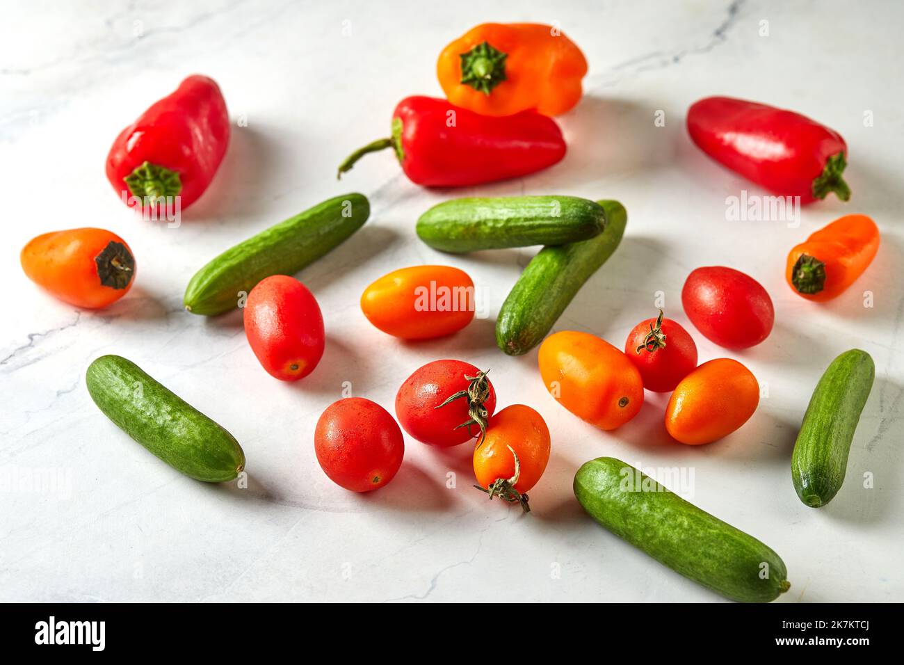 Mini verdure su marmo bianco pronte per cucinare e mangiare. Pomodori ciliegini, mini cetrioli e mini peperoni Foto Stock