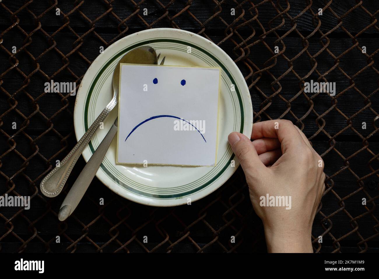 un piatto di carta su cui vengono disegnate una triste faccia sorridente e le mani femminili, fame e niente da mangiare, un cattivo umore a pranzo Foto Stock