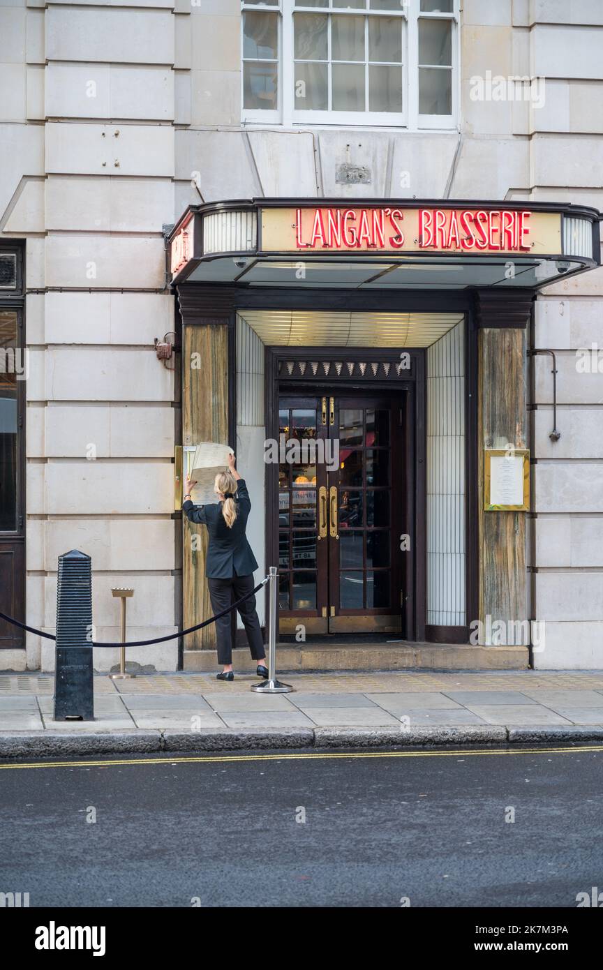 Giovane donna che cambia la vetrina del menu all'aperto al Langan's Brasserie. Stratton Street, Mayfair, Londra, Inghilterra, Regno Unito Foto Stock