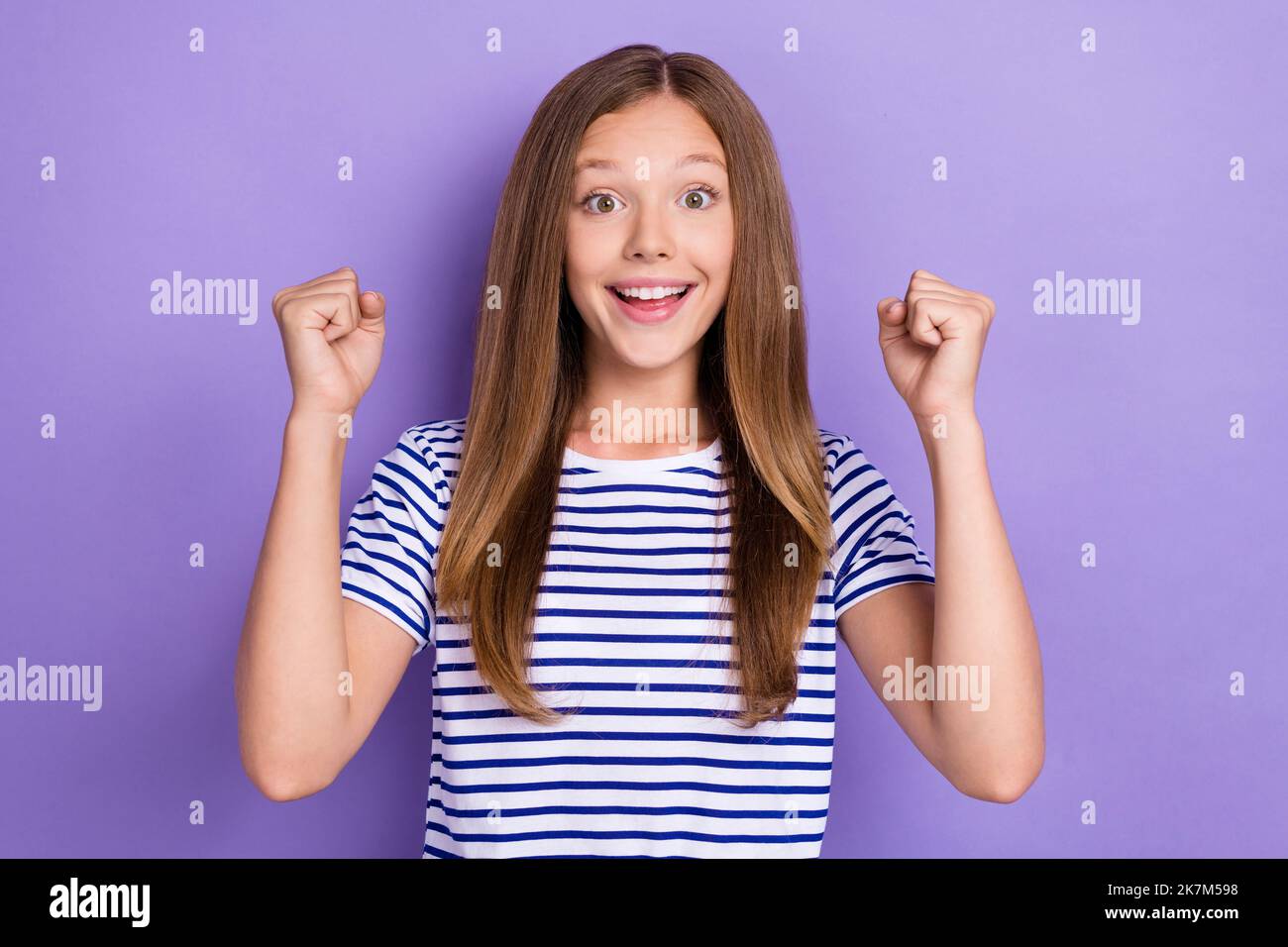 Foto di ragazza ottimista allegra positiva con capelli dritti vestiti t-shirt a righe clench pugni isolati su sfondo di colore viola Foto Stock