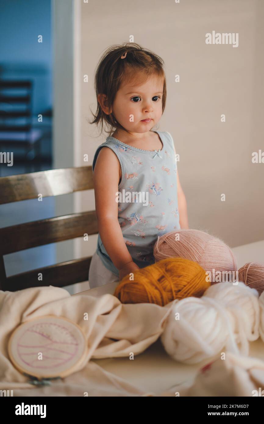 Ritratto di una ragazza adorabile in piedi al tavolo da lavoro pieno di attrezzi da ricamo in attesa che sua madre inizi l'attività del fine settimana. Bambina Foto Stock