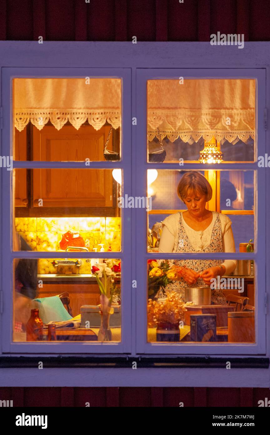 Una donna che lavora in una cucina vista attraverso una finestra di notte Foto Stock