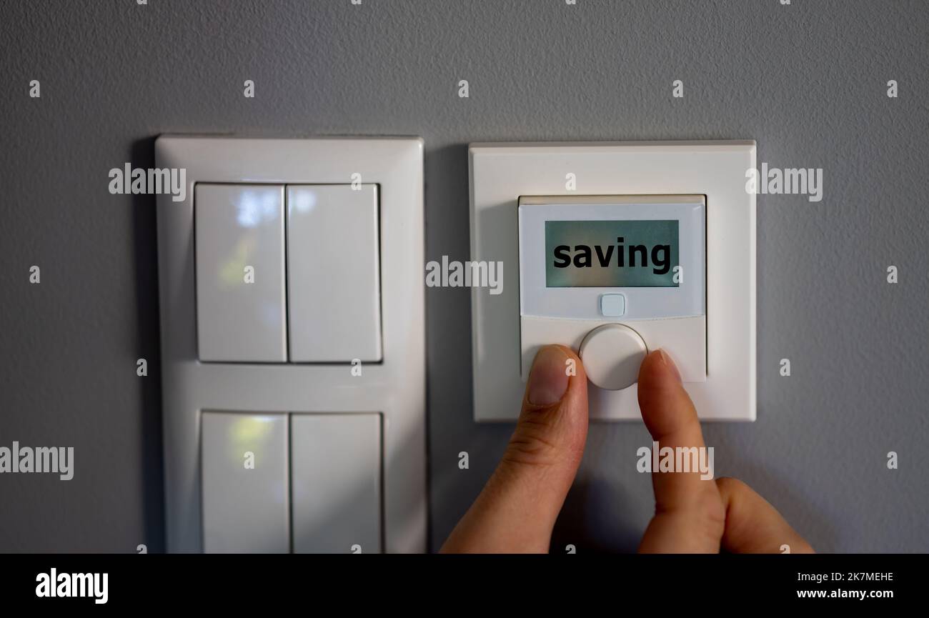 La mano modifica la temperatura su un termostato elettronico. Sul display viene visualizzata la parola salvataggio. Simbolo per il risparmio energetico. Foto Stock