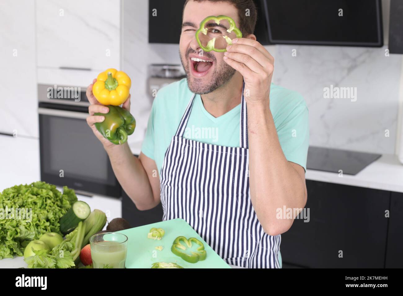 Uomo che gioca con peperoni verdi in cucina Foto Stock