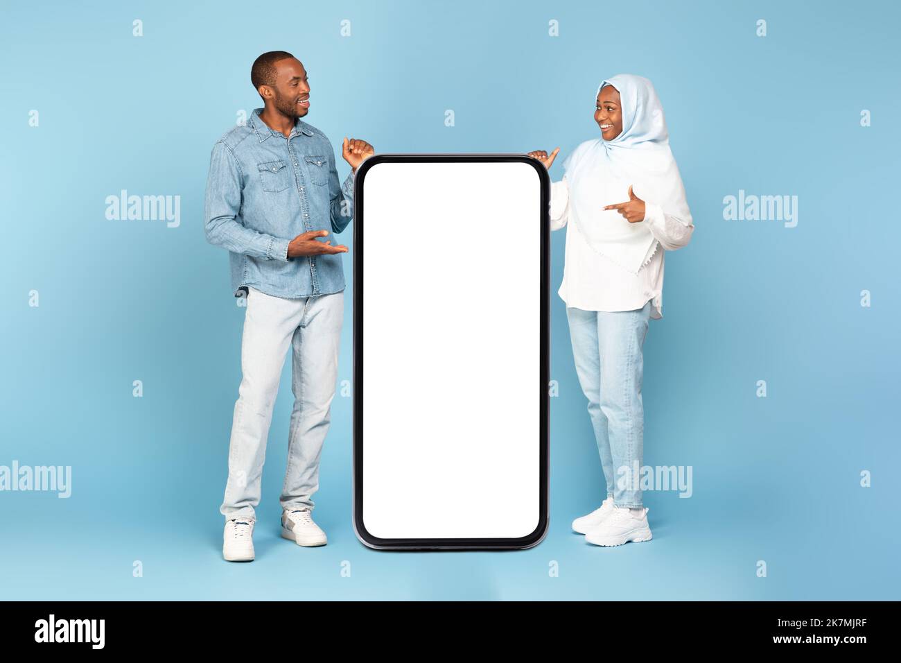 Sposi musulmani neri che puntano a grande schermo del telefono, sfondo blu Foto Stock