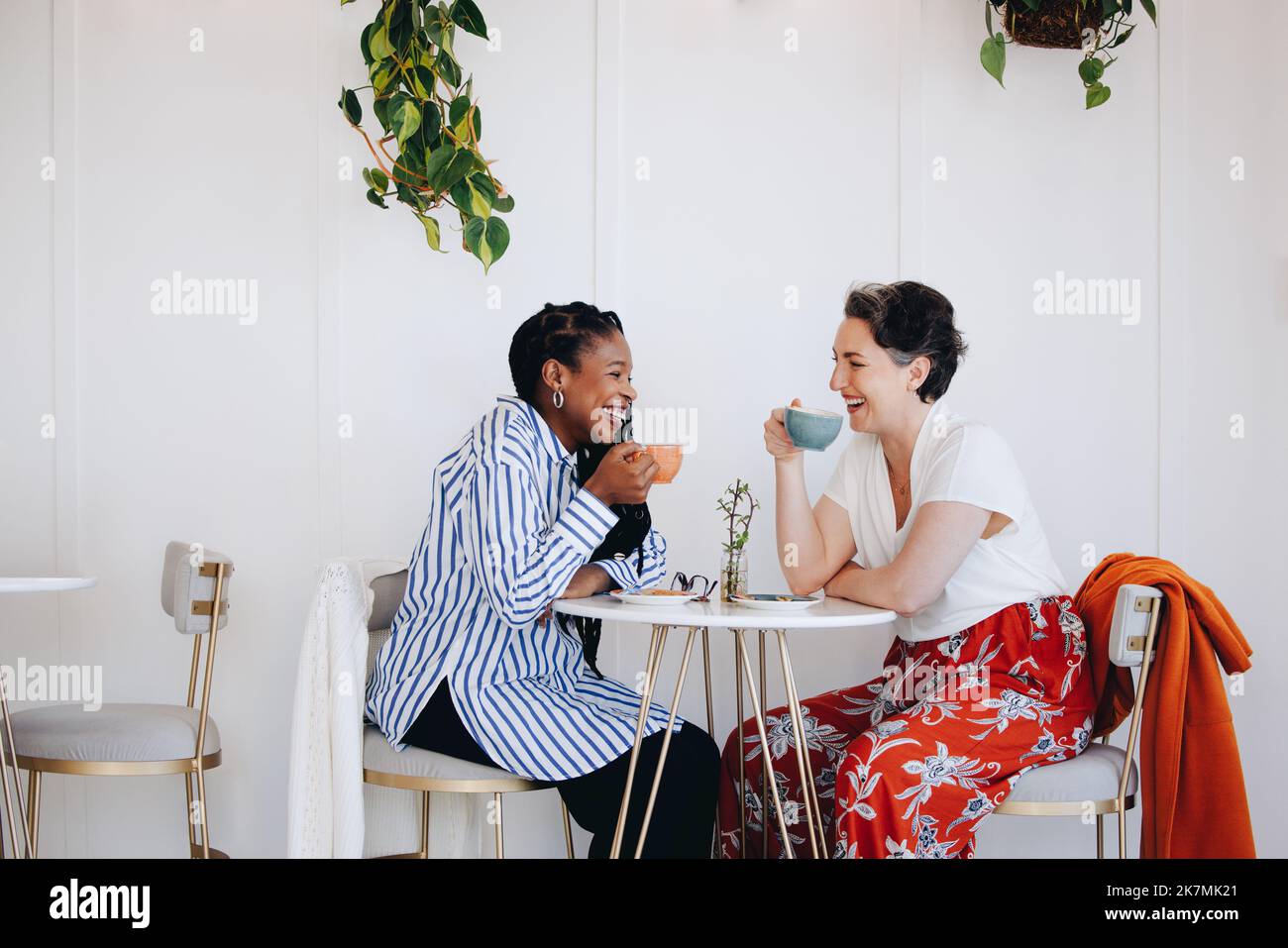 Allegre donne d'affari che ridono e che hanno caffè insieme in un caffè ufficio. Due donne d'affari felici che godono una pausa caffè insieme in un wor moderno Foto Stock