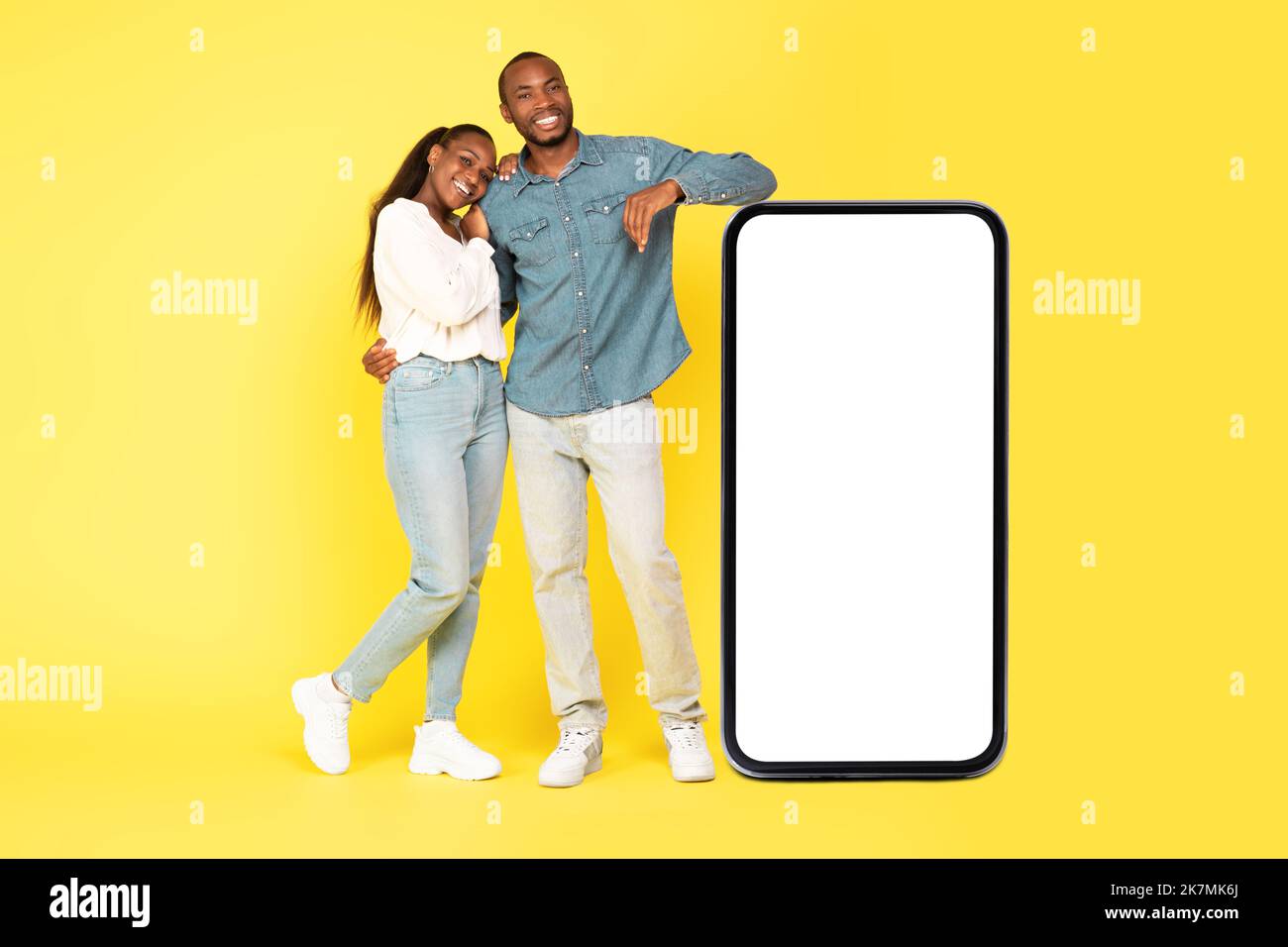 Coppia nera che abbraccia lo schermo del telefono grande su sfondo giallo Foto Stock