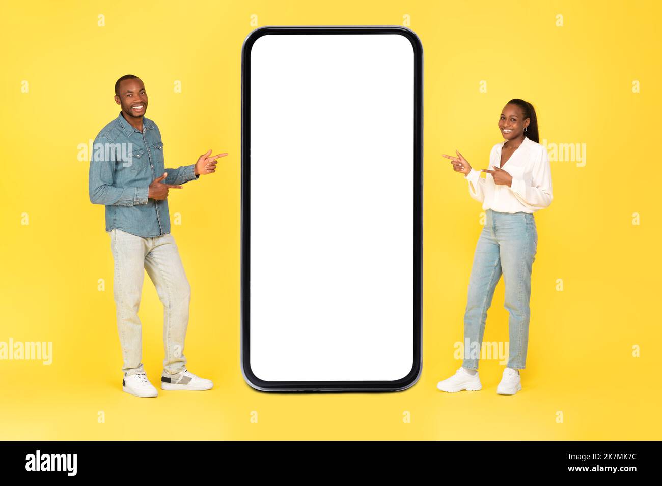 Coppia nera che mostra le dita puntate sullo schermo del telefono, sfondo giallo Foto Stock