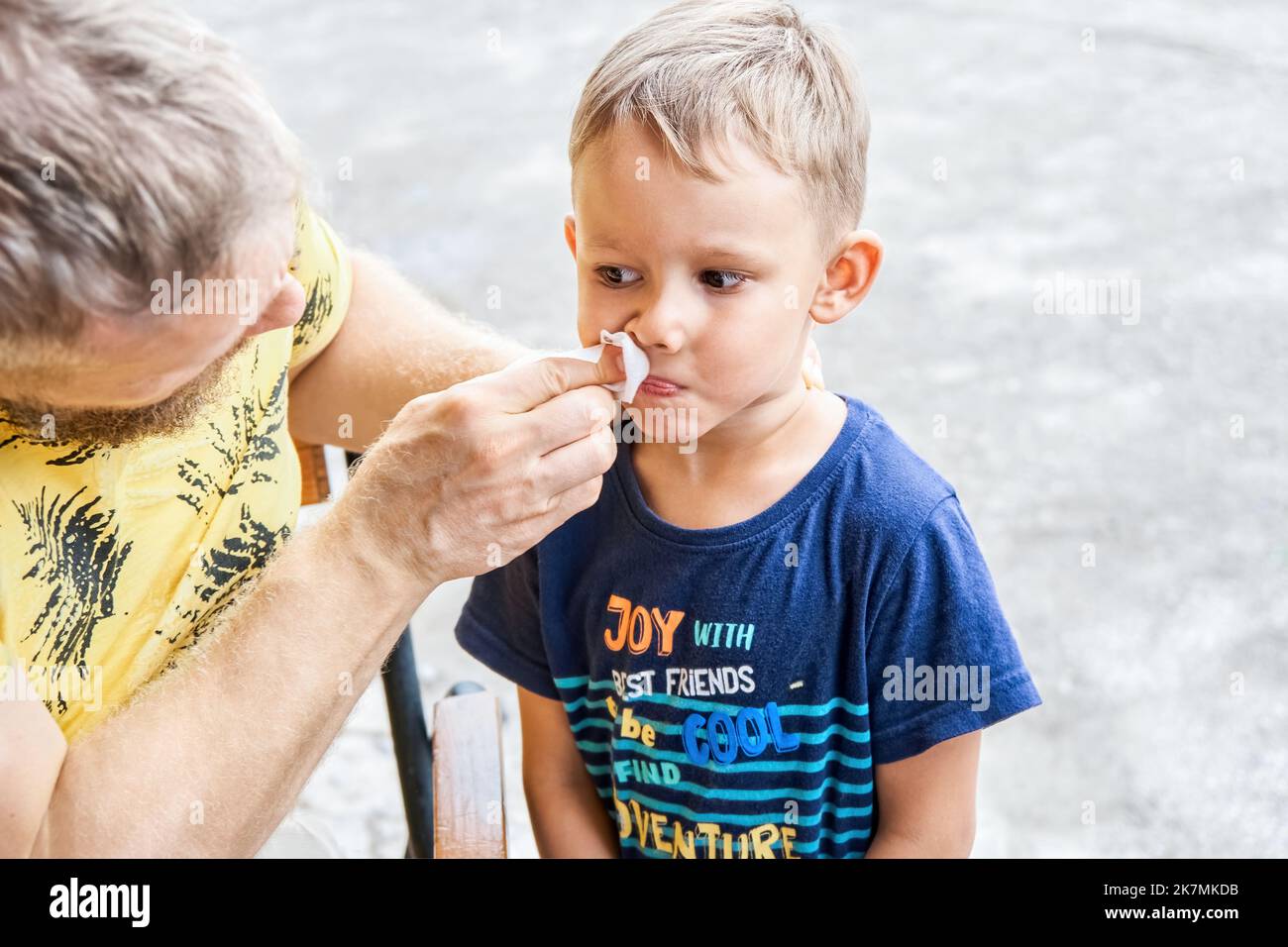 Padre pulisce il viso del ragazzo prescolare dai residui di gelato. I piedi del bambino di luce-haired che desiderano mangiare la dolcezza yummy closeup esterno Foto Stock