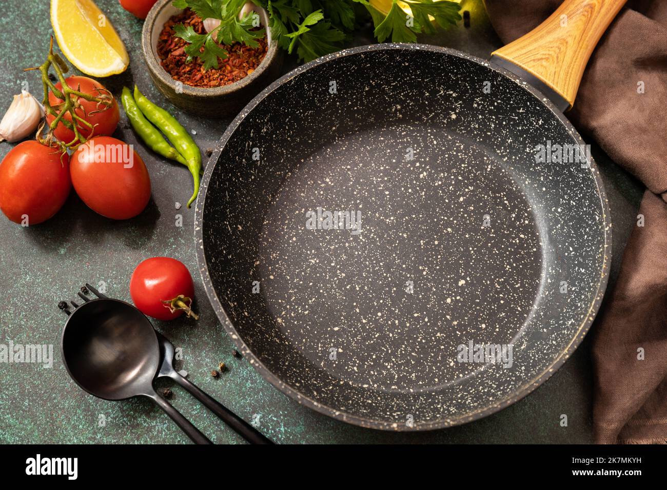 Cucina di fondo con padella. Padella vuota, verdure, spezie ed erbe su sfondo scuro del tavolo. Foto Stock