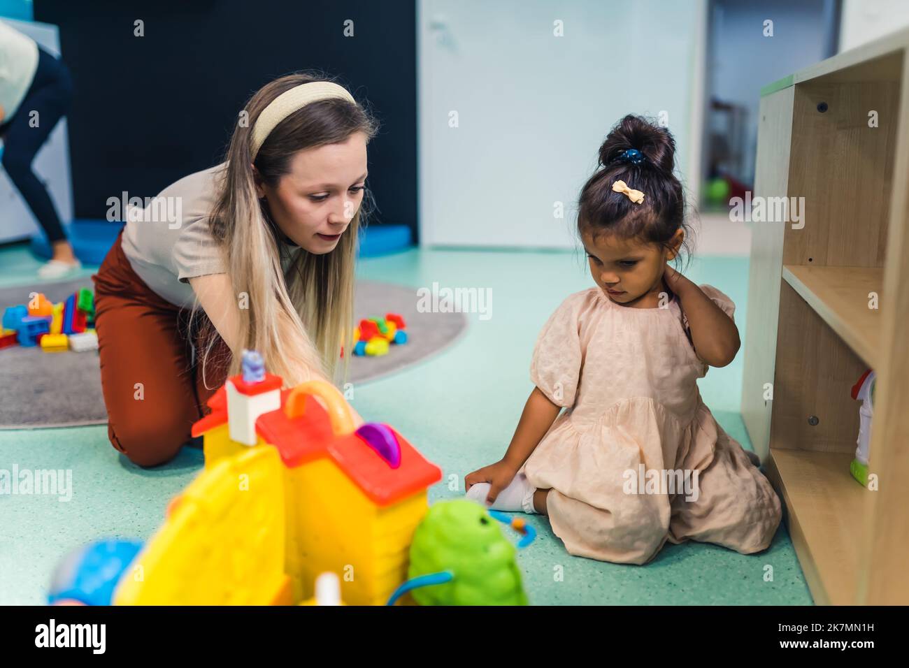 bella bambina e la sua insegnante che si divertono al vivaio, giocattoli sullo sfondo. Foto di alta qualità Foto Stock