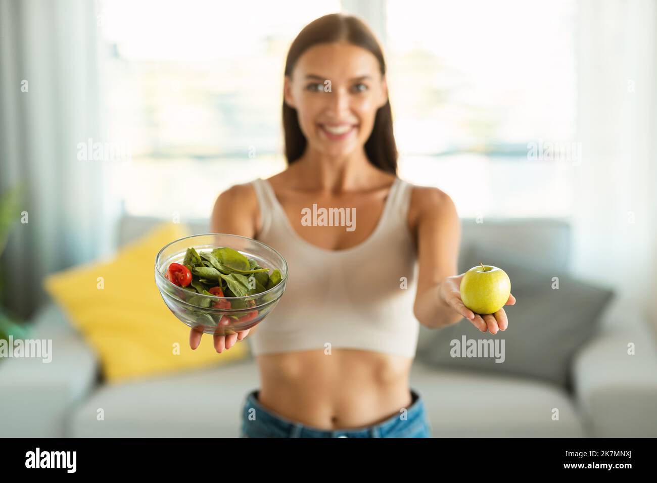 Donna felice che mostra insalata e Apple consiglia la dieta a casa Foto Stock