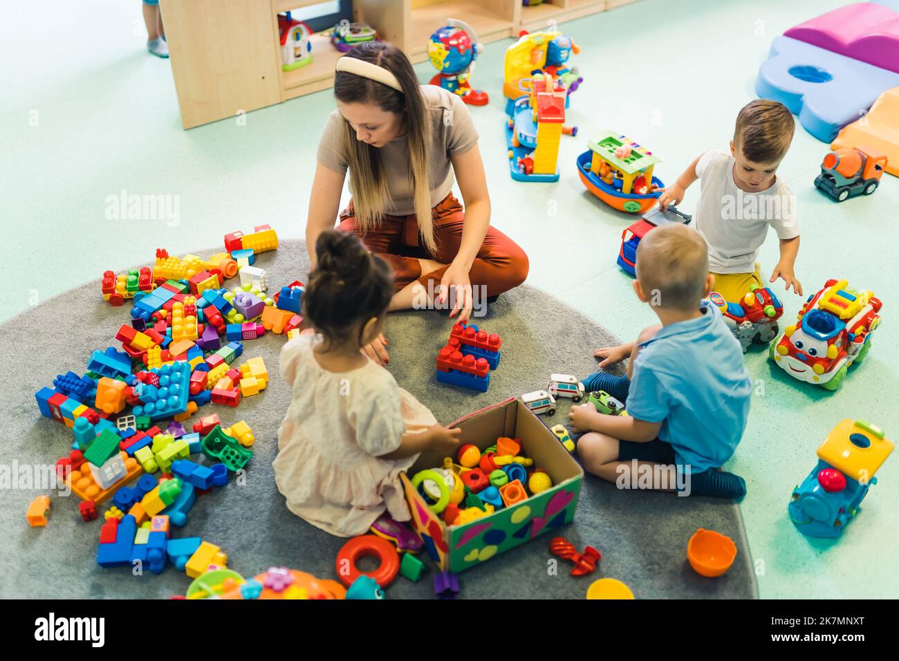 insegnante e tre preschoolers circondati dai giocattoli che giocano con i blocchi di costruzione all'asilo, giochi creativi per i bambini. Foto di alta qualità Foto Stock
