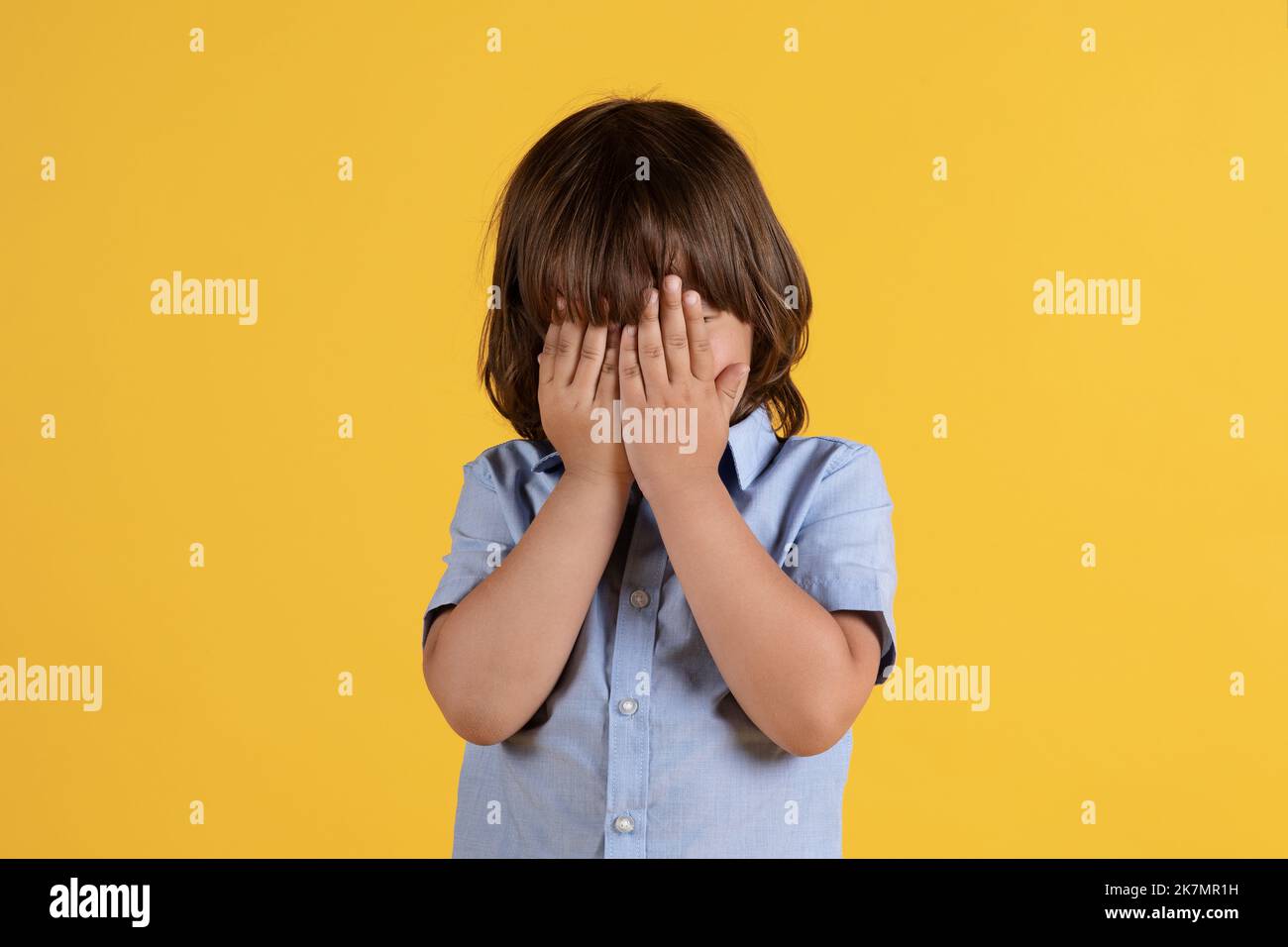 Offesa dei bambini. Primo piano ritratto di un ragazzino irriconoscibile che piange, coprendo il volto con le mani, sfondo arancione studio Foto Stock