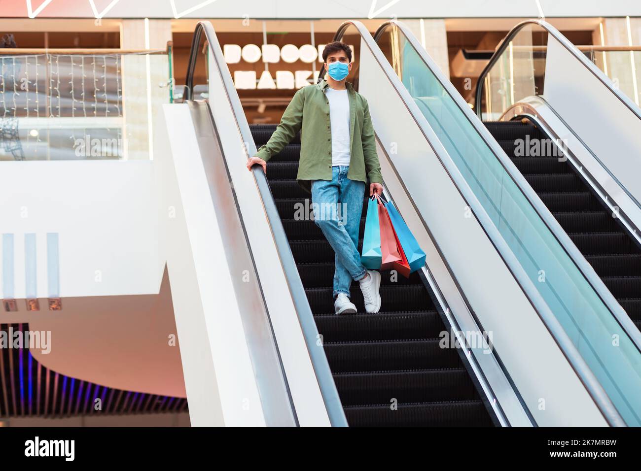 Guy in piedi su Moving Stairs Holding Shopper Bags in Mall Foto Stock