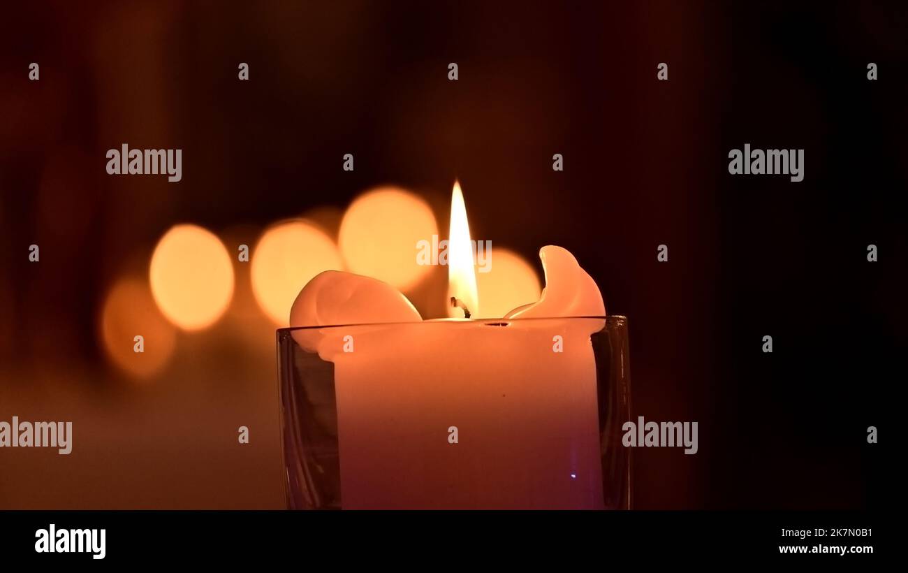 Primo piano di una candela in un bicchiere al buio con luci bokeh sullo sfondo Foto Stock
