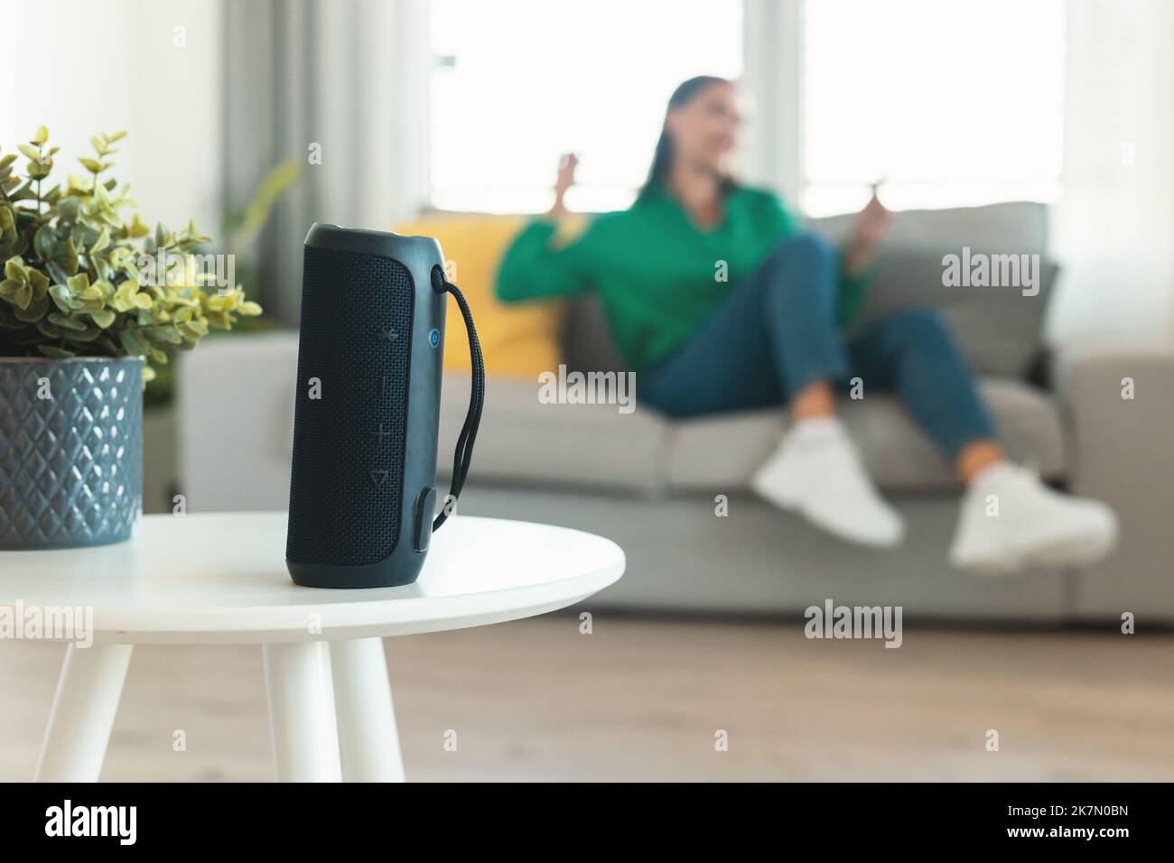 Altoparlante musicale in piedi sul tavolo mentre la donna ascolta la musica al chiuso Foto Stock
