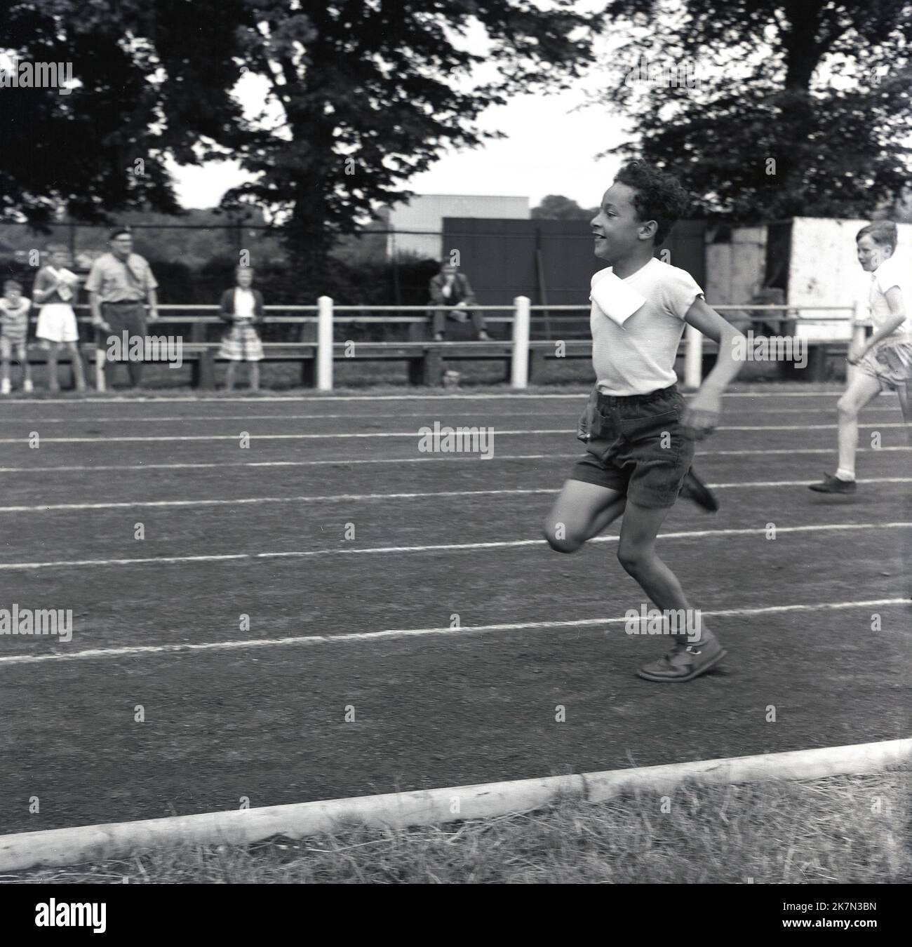 1960s, storico, fuori su una pista di cenere, due ragazzi in gara sprint running, Inghilterra, Regno Unito. Il ragazzo guida sta correndo nei sandali della sua scuola. Foto Stock