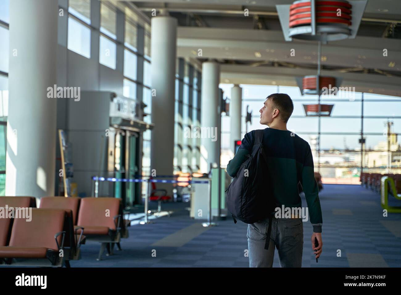 Vista posteriore dell'irriconoscibile viaggiatore maschio che cammina lungo l'aeroporto con zaino. Vista posteriore di un uomo che passa dal corridoio del terminal sulla via del volo Foto Stock