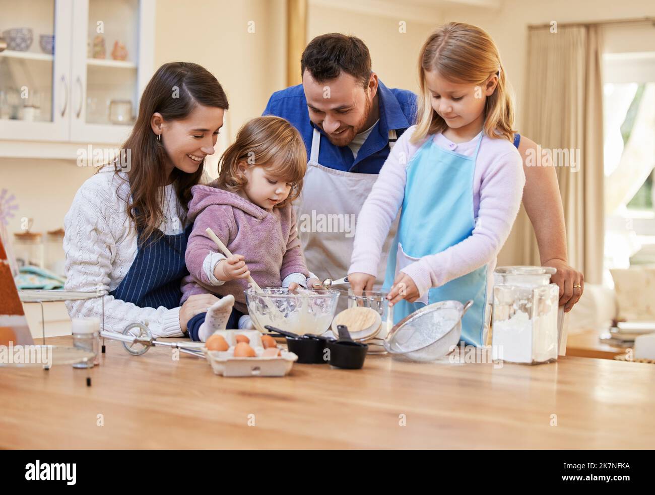 Aiutare le nostre ragazze a costruire un legame. una famiglia che cuoce insieme mentre una bambina agita una ciotola di pastella della torta. Foto Stock