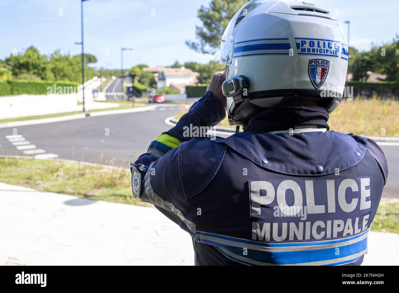 Ufficiale di polizia municipale del gruppo motore, visto da dietro, facendo una missione di sorveglianza con il suo binocolo sul lato della strada in un ar residenziale Foto Stock