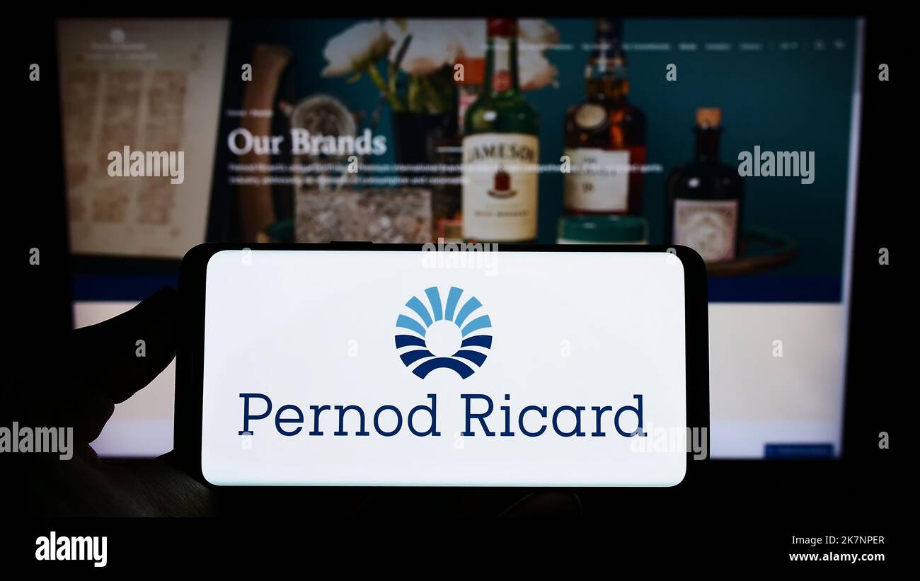 Persona che tiene il cellulare con il logo della società francese di bevande Pernod Ricard SA sullo schermo di fronte al sito web aziendale. Messa a fuoco sul display del telefono. Foto Stock