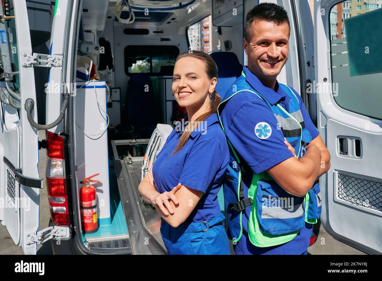 Squadra paramedica sicura in piedi vicino alla loro auto ambulanza con le braccia incrociate. Personale del servizio di emergenza Foto Stock