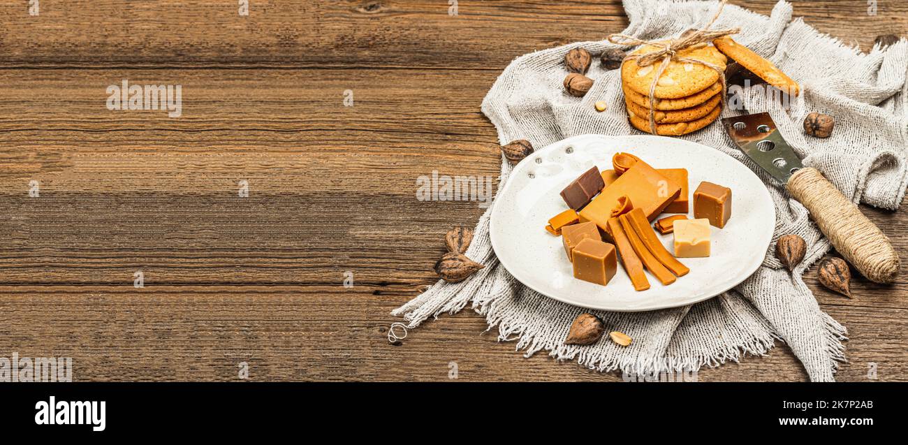 Brunost norvegese con biscotti e noci. Cibo sano e mangiare, ingrediente biologico per la prima colazione. Tradizionale formaggio marrone scandinavo, retro in legno Foto Stock